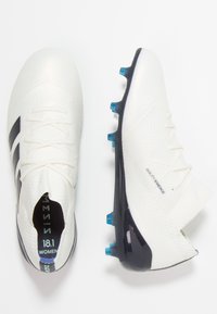 Botas de fútbol para mujeres blancas con una superficie texturizada, franjas negras y acentos azules, con un diseño elegante y cierre de cordones.