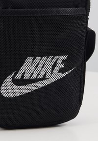 Černá texturovaná látková taška s bílým logem Nike vytištěným na přední straně na neutrálním pozadí.
