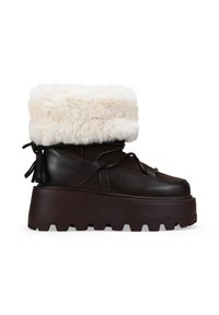 Botín de cuero marrón con puño de piel sintética, suela de plataforma y suela de goma texturizada. Presenta un cierre con cordones y borlas decorativas.