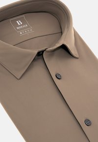 Camisa beige de botones, hecha de una tela suave, con un cuello clásico, dos botones negros en la parte delantera y una etiqueta con la marca "Boggi".