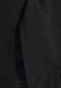 Černá, měkká, strukturovaná tkanina s žebrovaným lemem a švy, která vyniká bezproblémovou kombinací pohodlí a minimalistických designových prvků.