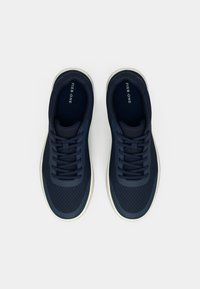 Ζευγάρι αθλητικά παπούτσια σε ναυτικό μπλε χρώμα με λευκές σόλες και κορδόνια, εμφανιζόμενα από πάνω σε απλό λευκό φόντο.