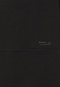 Tissu noir avec une couture horizontale et un petit logo gris « Marc O'Polo EST. IN STOCKHOLM » près de la couture sur le côté droit.