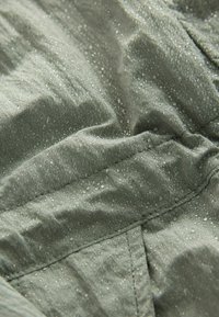 Tissu vert pâle, résistant à l'eau, texturé avec des gouttes visibles, présentant des détails de couture et une surface légèrement froissée.