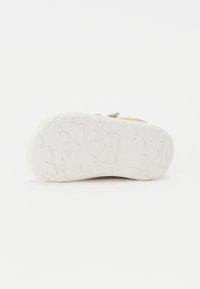 Semelle de chaussure en caoutchouc blanc avec un motif de bande de roulement texturé et le nom de la marque en relief. Zones légèrement surélevées pour l'adhérence, avec une finition lisse.