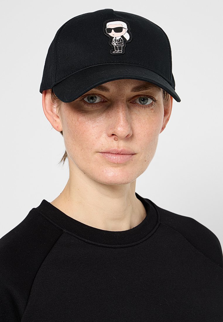Gorra negra de tela con un diseño estructurado, que presenta un logotipo de dibujos animados en la parte frontal. La gorra tiene un ala curva y una correa ajustable.