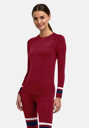 Kvinde iført tætsiddende bordeaux rullekrave og leggings med hvide og marineblå striber ved manchetter og lår, poserer mod en lys baggrund.