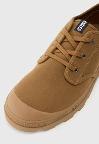 Bruine canvas sneakers met veters, rubberen neuskap en een gestructureerde zool. Heeft metalen oogjes en een klein merkenlabel op de tong.