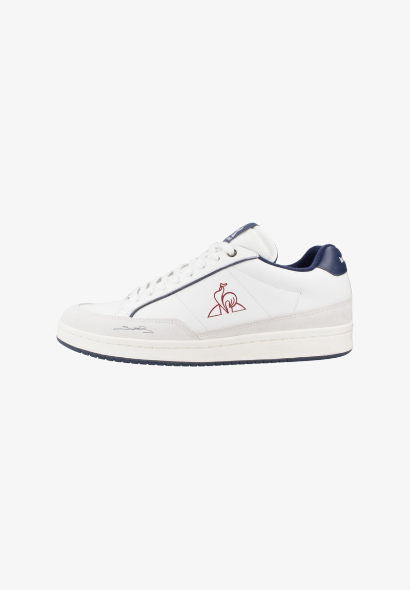 Zapatilla de cuero blanca con acentos en azul marino, textura suave, logo lateral y suela blanca. Presenta un sistema de cordones y un collar acolchado para mayor comodidad.