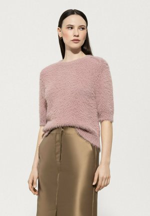 Rosa, flauschiger Kurzarmpullover mit Rundhalsausschnitt, kombiniert mit einem satinierenden goldenen Rock, der einen Schlitz vorne hat.