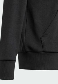 Sudadera negra con tejido texturizado, puños acanalados y un bolsillo lateral. El diseño es simple y con un corte relajado.