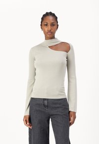 Haut à manches longues en rib ouatiné gris clair, avec un col montant et une découpe asymétrique sur une épaule, silhouette ajustée, texture douce.