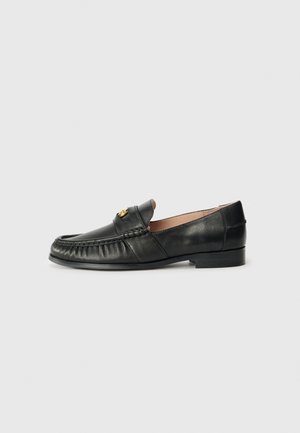 Black leather loafer with a rounded toe, featuring a stitched detail along the front and a small gold accent on the upper. Flat sole.
