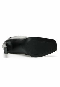 Svart läderankelboot med texturerad yta, fyrkantig tå, mönstrad design och en gummisula med horisontella spår.