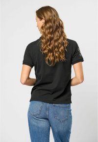Zwarte polo met korte mouwen en een getailleerd ontwerp. Kenmerkt zich door een zachte textuur en een klein embleem op de mouw. Gecombineerd met hoge, blauwe jeans.