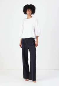 White, puff-sleeve top with a peplum waist, paired with high-waisted, navy wide-leg trousers. The fabric appears smooth and structured.