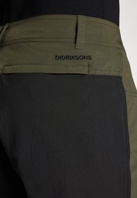 Mustard ja oliivrohelised püksid, millel on tekstuuriga viimistlus. Vöökoha peal on brodeeritud "Didriksons" logo. Omab sujuvat ja modernset disaini.