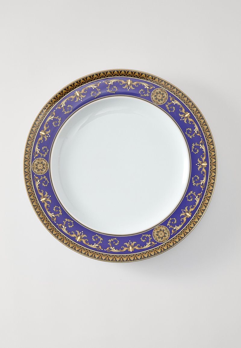 Zils un zelta rakstains porcelāna šķīvis ar gludu, baltu centru un izsmalcinātu dekoratīvu apmali ar ziedu un ģeometriskiem motīviem.