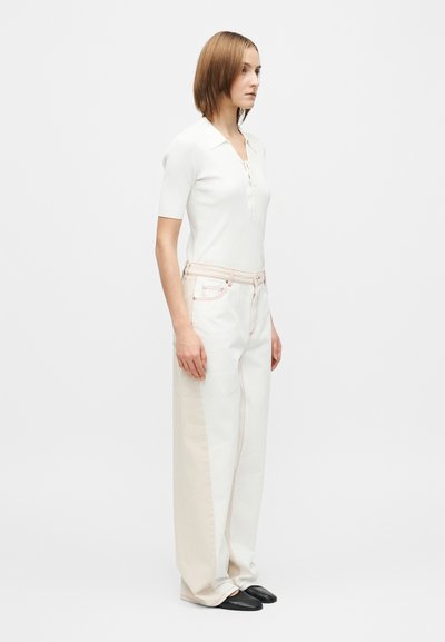 Vartalonmyötäinen valkoinen ribbineulospaita lyhyillä hihoilla, yhdistettynä korkeavyötäröisiin, väljämallisiin beigeihin ja valkoisiin housuihin, joissa on kontrastisaumat. Mustat kengät.