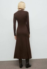 Vestito marrone a maniche lunghe con una silhouette aderente, tessuto morbido e orlo svasato. Presenta arricciature decorative lungo il lato.