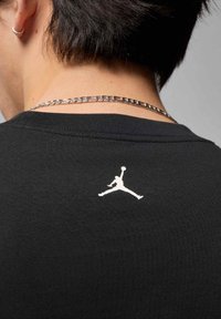 Czarna bawełniana koszulka z białym logo Jumpman na plecach, tuż przy linii szyi. Do kompletu dołączony srebrny łańcuszek.