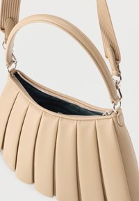 Μπεζ πλεκτή τσάντα χειρός με κλείσιμο με φερμουάρ, δερμάτινη λαβή και ρυθμιζόμενο υφασμάτινο λουρί ώμου, εμφανιζόμενη ημι-ανοικτή.