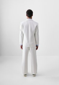 Weißer Anzug mit einem maßgeschneiderten Blazer und weit geschnittenen Hosen, gefertigt aus glattem Stoff, mit klarer Silhouette und subtilen Nahtdetails auf der Rückseite.