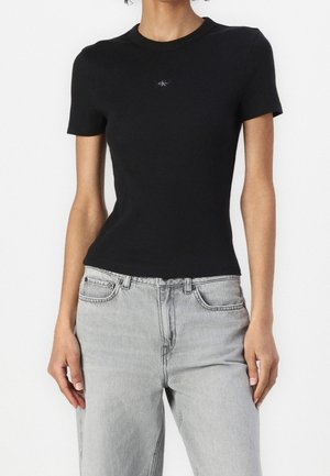 Czarny prążkowany t-shirt z krótkim rękawem o dopasowanym kroju i małym logo na piersi, w połączeniu z jasnoszarymi dżinsami.