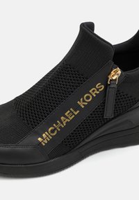Sorte slip-on sneakers med strukturelt mesh-overdel, detalj i gulltone med logo og en kileplattform såle for ekstra høyde og komfort.