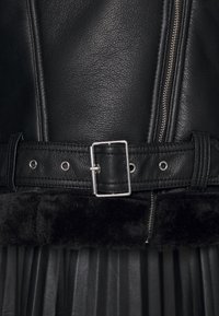 Zwarte leren jacket met een zilveren gesp riem, ritsluiting, textuurstof en een zachte zwarte afwerking aan de onderrand.