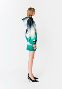 Sudadera con capucha en degradado de teal a negro con tela texturizada, combinada con una falda corta a juego y zapatos de tacón alto negros.