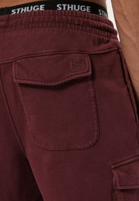 Pantalones cortos tipo cargador burdeos con cintura elástica, que cuentan con un bolsillo trasero con un logotipo sutil y un tejido suave y texturizado.