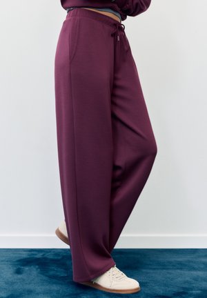 Pantaloni ampi color marrone scuro realizzati in tessuto morbido, con vita elastica e coulisse, tasche laterali, abbinati a sneakers beige.