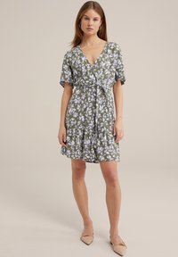 Rochie înflorată de tip wrap, de culoare verde măsliniu, cu modele albe și lavandă. Are mâneci scurte, talie legată și fustă în straturi.