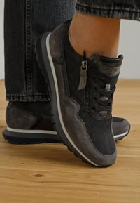 Schwarze und graue Sneakers bestehen aus einer Mischung aus Wildleder und Mesh-Materialien, verfügen über ein Reißverschlussdetail und haben eine weiße Zwischensohle mit einer strukturierten schwarzen Außensohle.