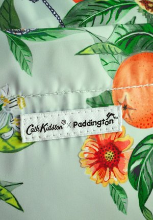 Auduma ar ziedu rakstu, kurā ir oranžas, sarkanas un zaļas pēdas. Satur balto etiķeti ar "Cath Kidston x Paddington" zīmoljumu.