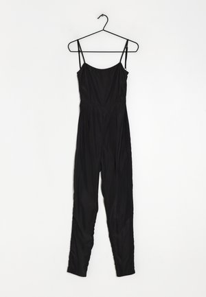 Schwarzer Jumpsuit mit dünnen Trägern, figurnahem Oberteil und zulaufenden Beinen. Aus glattem Stoff gefertigt, mit tailliertem Bund und ohne sichtbare Verschlüsse.
