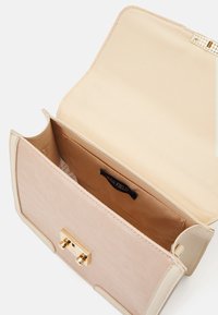 Beige crossbody-väska med krokodilstruktur, guldvridspärr och tygfoder med en etikett i innerfickan.