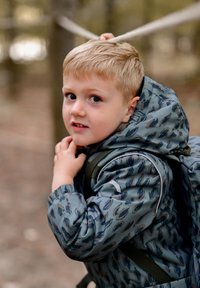 Grå mønstret dunjakke med hætte, med diskrete blå og brune accenter. Barnet holder i et reb, med en rygsæk synlig.