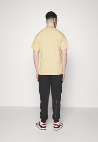 Beige bomulls t-shirt med korta ärmar, matchad med svarta cargobyxor med sidofickor och textdetalj, bärs med vita och röda sneakers.