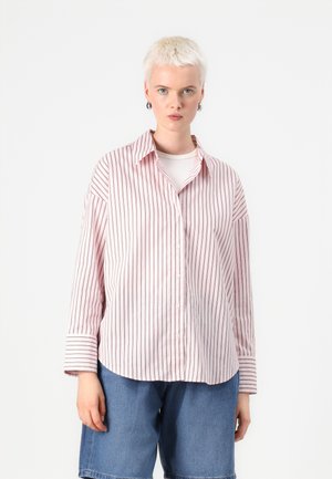 Lys rosa skjorte med vertikale røde striper, lange ermer og klassisk krage, sammen med denimshorts. Myk, glatt tekstur.