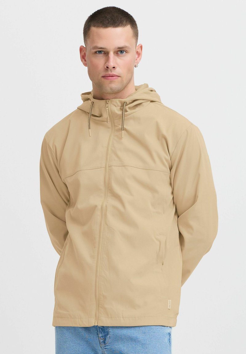 Khaki jacket with a hood, featuring a zip front, drawstring closure, and smooth fabric. Accented with a horizontal seam across the chest.