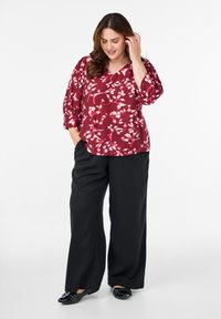 Marjatan kukkakuosiset pusero, jossa on V-kaulus ja kolmanneksen pituiset puffihihat, yhdistetty mustiin leveälahkeisiin housuihin ja kiiltäviin mustiin balettitossuihin.