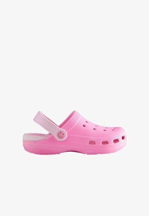 Ružové dreváky z umelého materiálu, s tlačidlom na popruhu v tvare usmievajúcej sa tváre, ventilačnými otvormi a bielou podrážkou.