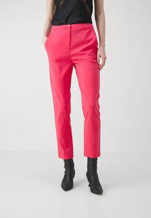 Fuksia muotihousut slim fit -tyyliin, joissa on sivutaskut ja litteä etumuksen. Yhdistetty mustiin nilkkureihin, korostaen modernia siluettia.