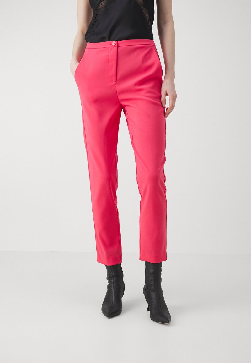 Fuksia muotihousut slim fit -tyyliin, joissa on sivutaskut ja litteä etumuksen. Yhdistetty mustiin nilkkureihin, korostaen modernia siluettia.