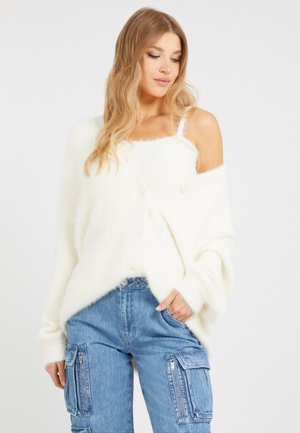 Fluffy, oversized white cardigan with buttons, worn over a white tank top. Paired with light blue cargo pants featuring zip pockets.