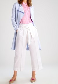 Světle modrý dlouhý kabát, růžová košile s kostkovaným vzorem, bílé kalhoty širokého střihu se stahovací šňůrkou a r�ůžové baleríny s mašlí. Hladké textury a uvolněný fit.