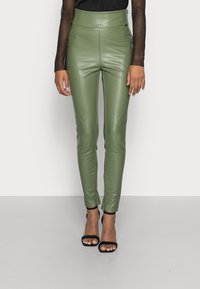 Pantalones ajustados de imitación cuero verde con cintura alta, con una textura suave y un diseño elegante, combinados con tacones negros con tiras.