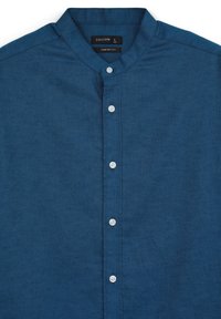 Camicia casual blu con colletto stondato, caratterizzata da un tessuto a trama e cinque bottoni bianchi sul fronte. L'etichetta riporta "CALLIOPE" e la taglia "L."